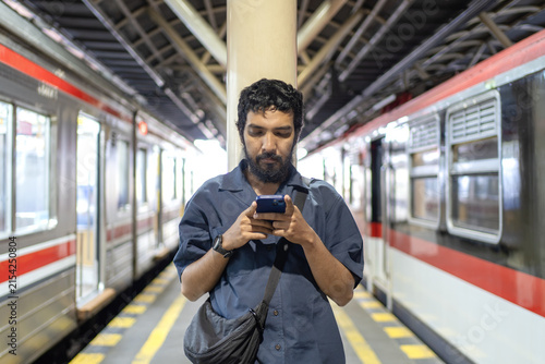Male commuter using smartphone between trains at a railway station