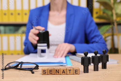 Quadro su tela In a bright office filled with yellow folders, a person prepares important documents while tiny figures represent senators