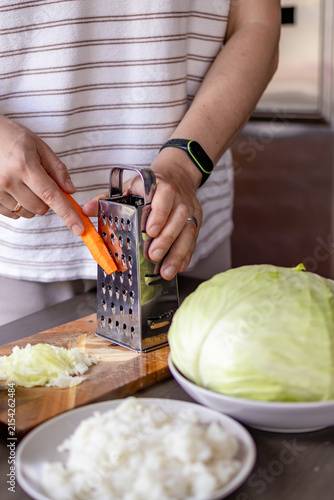 Man grates carrots beside cabbage and other ingredients while preparing homemade cabbage rolls. Concept of shared kitchen work,  meal preparation, family recipes and cooking skills