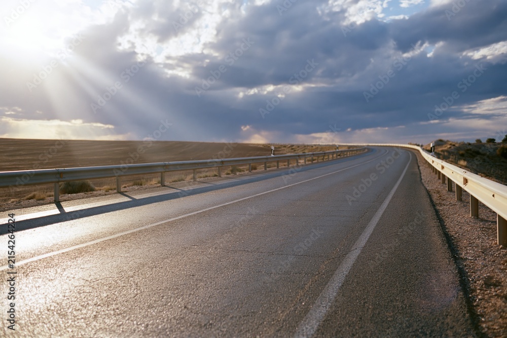 Obraz premium The Road Under Sunlit Sky: Serene Desert Highway Stretch at Dusk