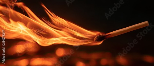 A burning matchstick ignites in a swirl of bright orange flames against a dark background