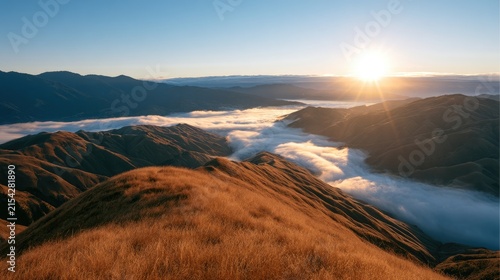 Golden sunrise illuminates misty valleys between rolling, grass-covered hills