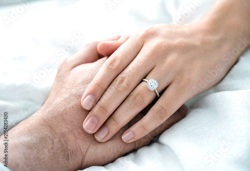 Closeup of two hands gently holding each other with a sparkling diamond engagement ring visible