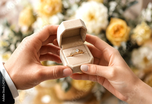 Closeup of hands holding an open ring box with an engagement ring surrounded by flowers