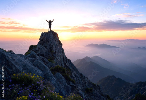Silhouette of a person standing on a mountain peak with raised arms at sunrise