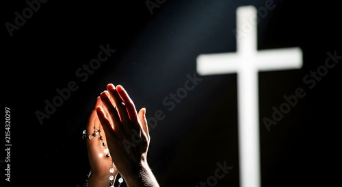 Hands in prayer with illuminated cross in dark background
