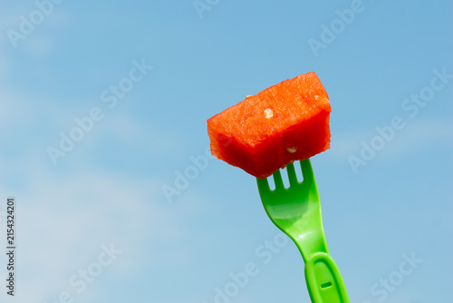 Konstfotografi A piece of fresh juicy watermelon on a green plastic fork held by a hand against