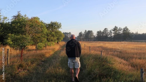 Hirtshals, Denmark A man walks in the early morning on a dirt road with lush fields. 