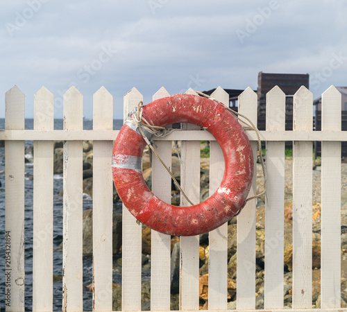 Weathered red lifebuoy hanging on wooden fence.