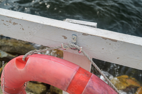 Pink lifebuoy tied to weathered white railing by water.