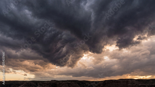 Quadro su tela Intense and textured dark storm clouds loom dramatically over an arid desert landscape at sunset