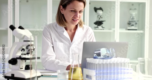 In a bright and clean laboratory, a dedicated scientist focuses on her laptop as she analyzes data. Surrounded by equipment and test samples, she is immersed in her research at work.