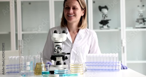 A cheerful researcher stands in a modern lab, surrounded by glassware and a microscope. With a smile, they prepare for an exciting experiment in the vibrant space.