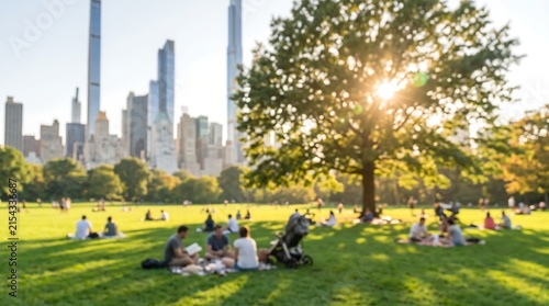 Golden hour sun rays filtering through large tree in Central Park with blurred city skyline and people enjoying picnic on lawn during warm summer afternoon in New York City
