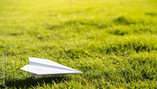 Photography of a folded white paper airplane resting peacefully on green meadow grass copy space