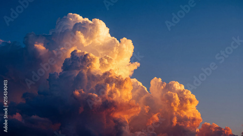 Quadro su tela Dramatic, towering cumulus clouds brilliantly illuminated by golden sunlight against a deep blue sky