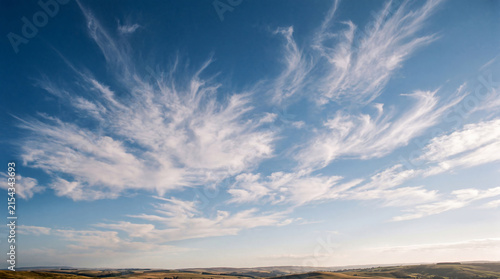 Canvas Print Expansive blue sky filled with gracefully sweeping cirrus clouds above a sunlit rolling landscape
