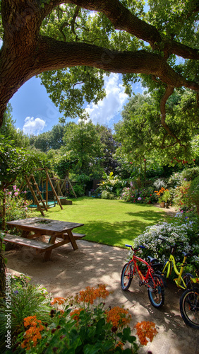 A cozy backyard garden with shady trees, swings, a playhouse, and a place for children to relax and play.