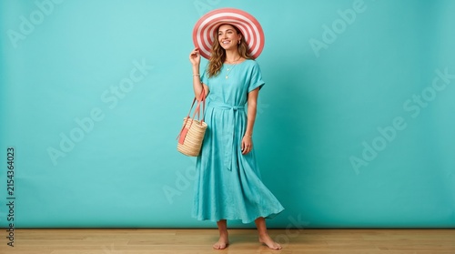 Happy woman in summer dress and sun hat posing against blue background.