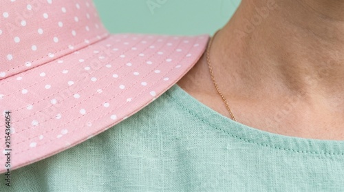Minimalist close up of woman wearing pink polka dot hat and green shirt.