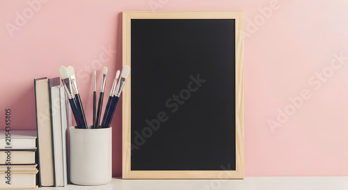 Blackboard with art supplies and books on a pink wall for creative concepts