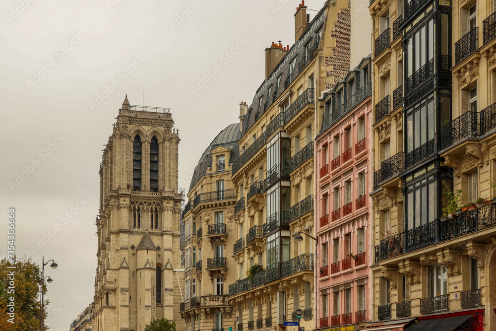 Obraz premium Notre Dame Cathedral tower rising above classic Haussmann buildings and a colorful pink facade in Paris, France