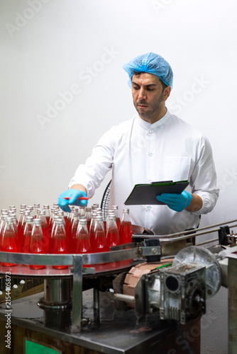 Portrait of mature male researcher with bottle of red beverage in bottle factory.