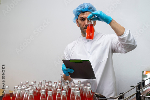 Portrait of mature male researcher with bottle of red beverage in bottle factory.