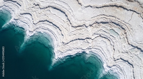 Dead Sea salt crystals edge vivid deep blue-green water in extraordinary white patterns in 19:6 ultra-wide nadir — Earth's lowest point as panoramic aerial art.