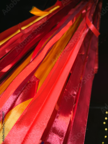 Abstract background of vibrant red, orange, and yellow satin ribbons hanging vertically, creating a festive, fiery texture with warm light leaks on a dark background.	