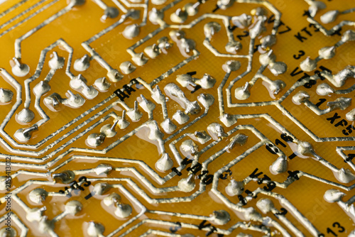 Macro photography of solder joints and copper tracks on a yellow printed circuit board. Technical background of electronic pathways and manual soldering work.	