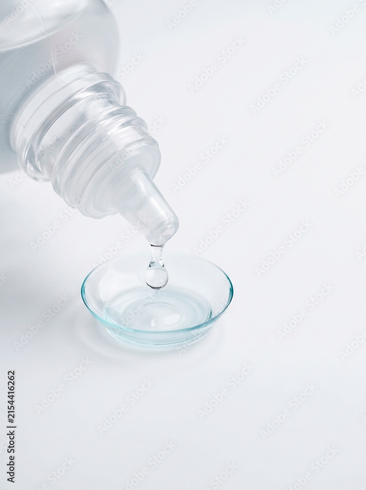 Fototapeta premium Contact lens care solution dripping into clear contact lens on white background, vision care and optical hygiene concept