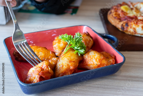 Fork stabbing roasted barbecue chicken wing in red ceramic dish on wooden table.