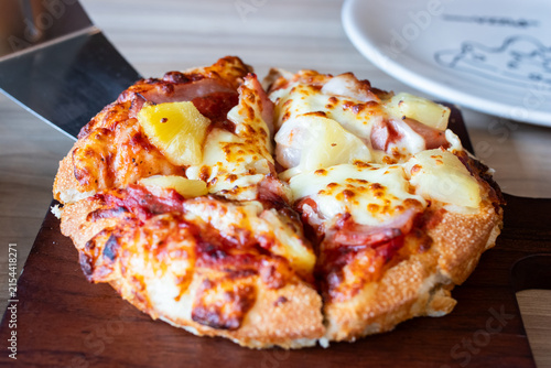 Lifting a slice of Hawaiian pizza with melted cheese pull and pineapple toppings using metal spatula.