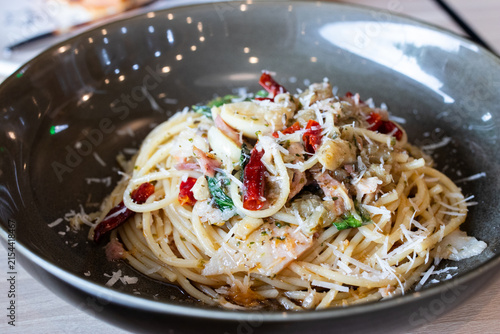Spaghetti aglio e olio with bacon dried chili and grated parmesan cheese served in deep grey ceramic bowl.