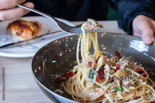 Fork lifting spaghetti aglio e olio with bacon dried chili and parmesan cheese from deep bowl. (