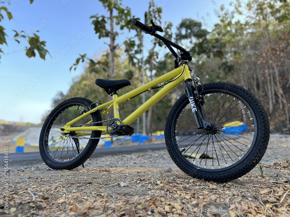 Fototapeta premium Yellow BMX bicycle photographed beside a countryside road near a tropical teak forest from a low front angle under sunny skies.