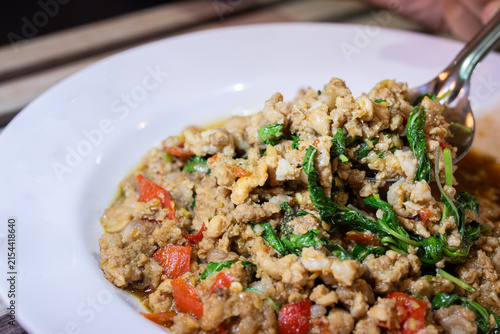 Spoon scooping stir fried minced pork with holy basil pad kaprao served on white plate.