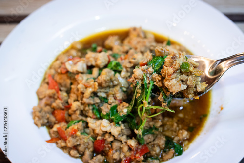 Spoon scooping stir fried minced pork with holy basil pad kaprao served on white plate.