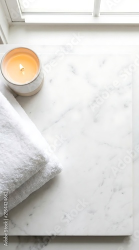 Top-down spa scene with folded white towels and a lit ceramic candle on white marble. Soft window light creates a clean, minimal, and tranquil wellness vibe.