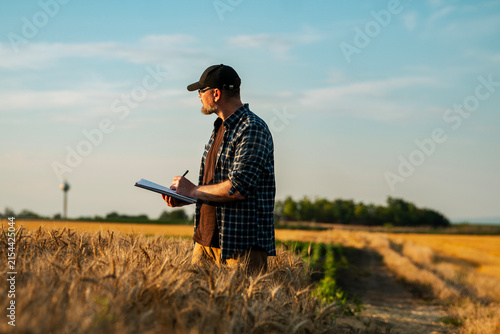 Middle aged male farmer standing in a field and writing notes on a paper clipboard