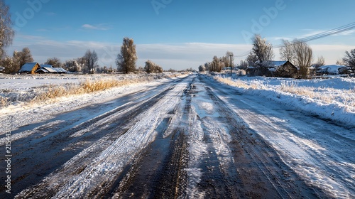 Rural winter road with melting snow and distant frosted houses