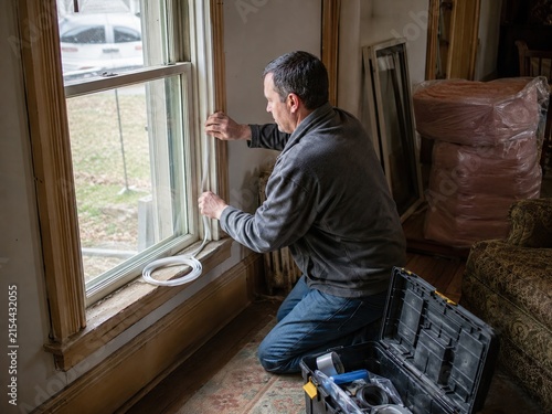 Homeowner installing weather stripping on old window