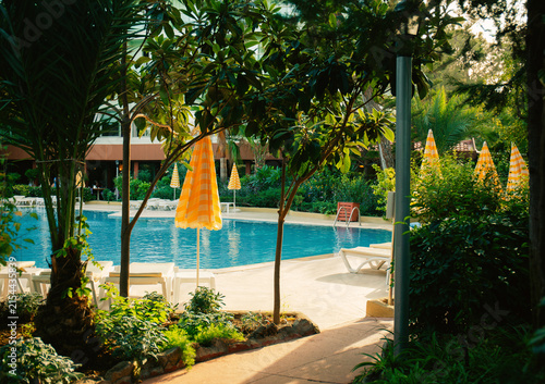 Outdoor swimming pool with blue water, empty sun loungers and yellow striped umbrellas. Luxury resort hotel relaxation zone, summer vacation concept.	

