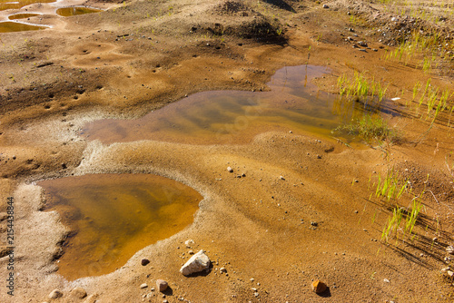 Canvas Print Drying mud puddles with murky water on a desolate sandy quarry floor surrounded