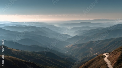 Winding Mountain Road Overlooking Layers of Misty Blue Peaks Under a Soft Morning Sky