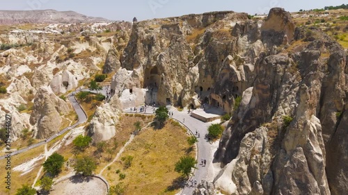 Goreme, Nevsehir, Turkey. Goreme Open Air Museum, ancient rock-cut churches and monastic caves in volcanic tuff, aerial view with tourists exploring under bright summer sun. Aerial View, Point of int