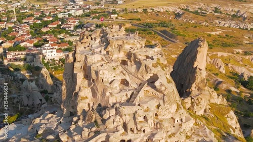 Uchisar, Nevsehir, Turkey. Uchisar Castle, the tallest fairy chimney in Cappadocia, its honeycomb of rock-carved rooms and tunnels glowing in warm morning light, aerial close view. Aerial View, Maste