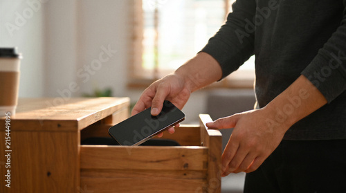 Person putting a smartphone away inside a wooden drawer at home, symbolizing digital detox, reduced screen time, disconnection and healthier everyday habits.
