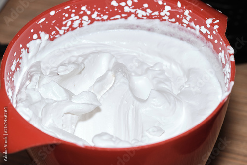 Close-up of freshly whipped cream inside a red plastic mixing bowl on a table